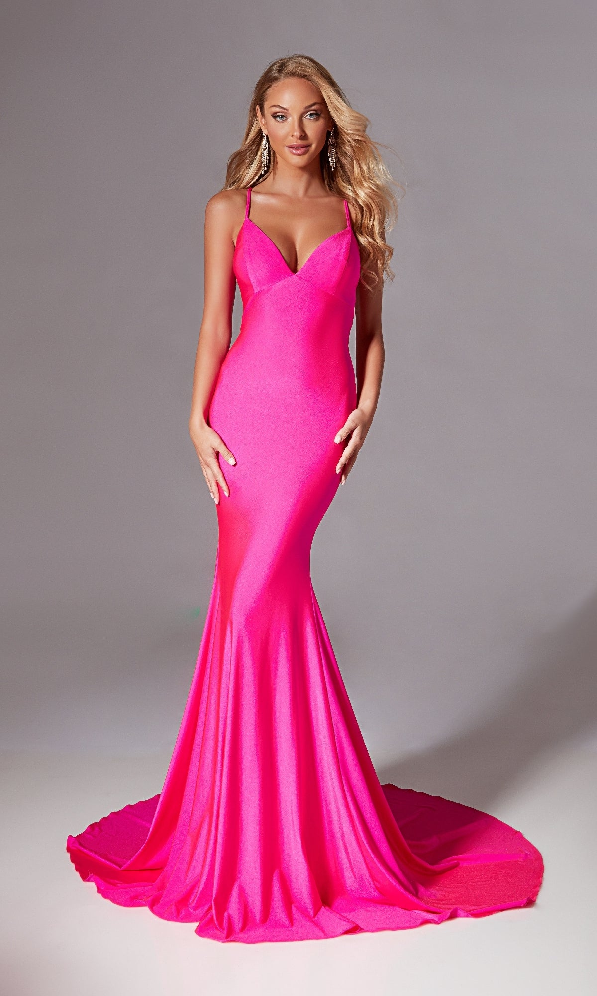 A woman models the Aerie Couture 212 Strappy Long Mermaid Prom Dress in bright pink, featuring spaghetti straps and a floor-length fitted silhouette, standing before a plain gray background.